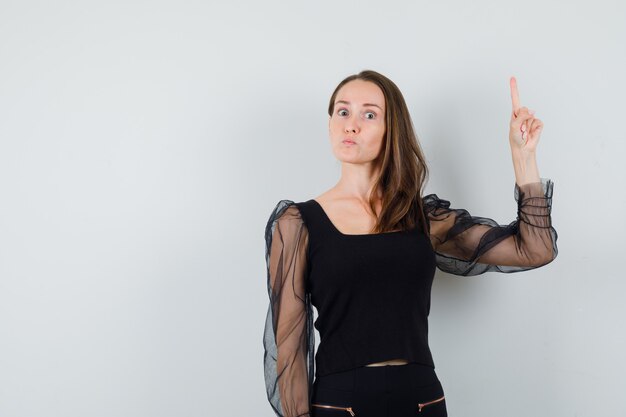 Young woman pointing up in black blouse and looking concentrated 