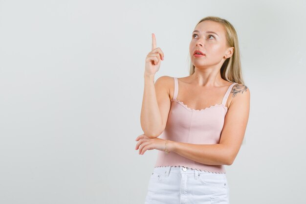 Young woman pointing up finger in singlet, mini skirt 