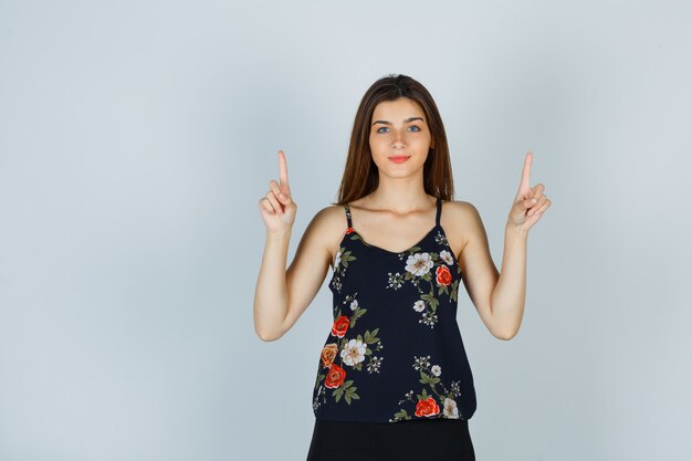 Young woman pointing up in floral top and looking confident