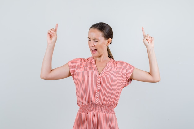 Young woman pointing up and shouting in striped dress , front view.