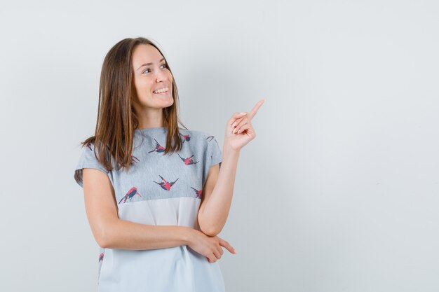 Young woman pointing up in t-shirt and looking blissful. front view.