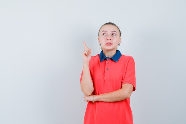 Young woman pointing up in t-shirt and looking curious