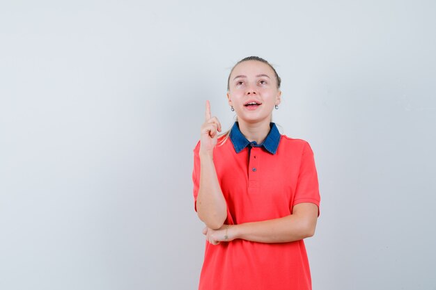 Young woman pointing up in t-shirt and looking hopeful