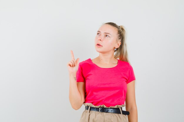 Young woman pointing up in t-shirt and pants and looking focused