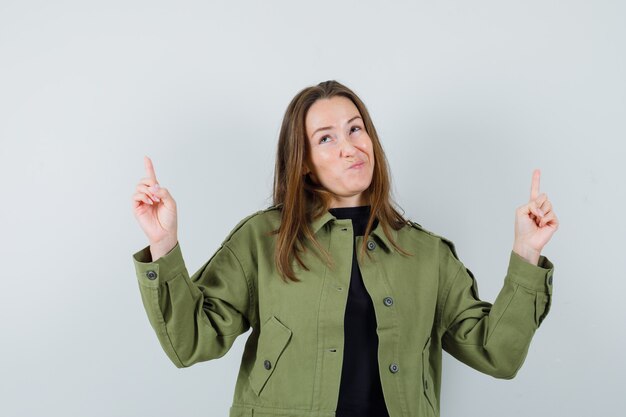 Young woman pointing up while pouting her lips in green jacket front view.