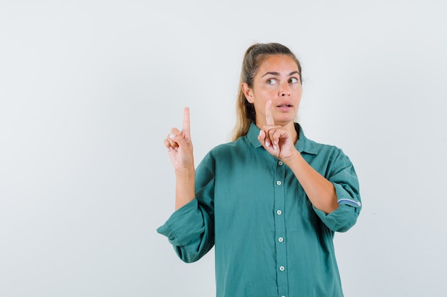 Young woman pointing up with index fingers in green blouse and looking attractive