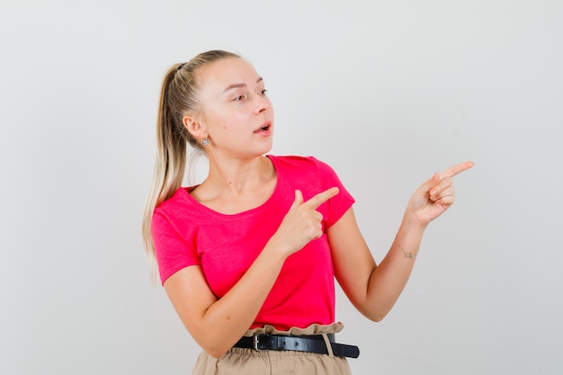 Young woman pointing at upper right corner in t-shirts and pants and looking focused