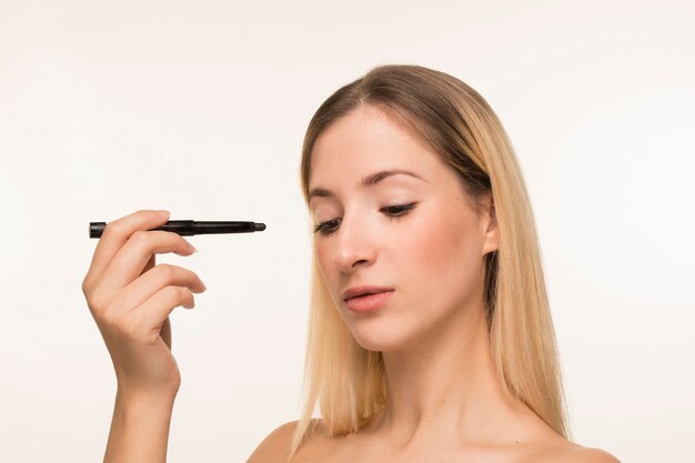 Young woman pointing with eyeliner towards her face