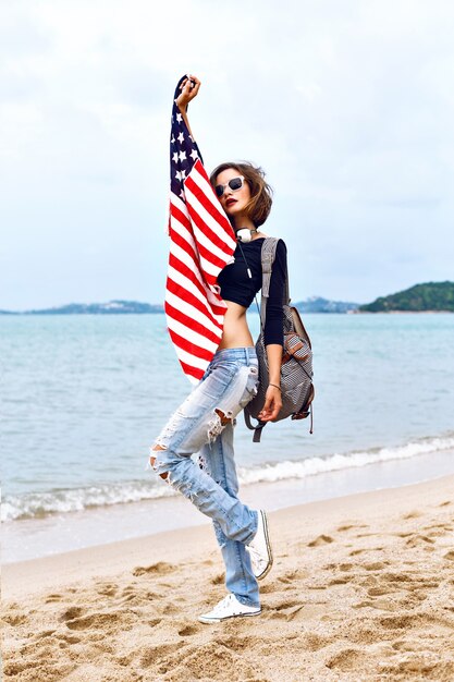 Young woman posing at the beach listening music in her stylish big headphones