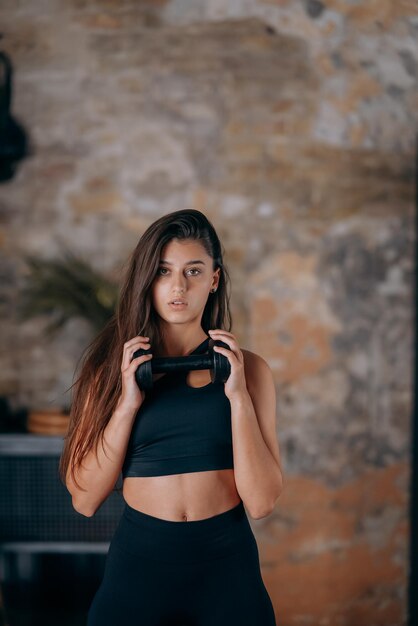 Young woman posing at the camera with dumbbells in her hands