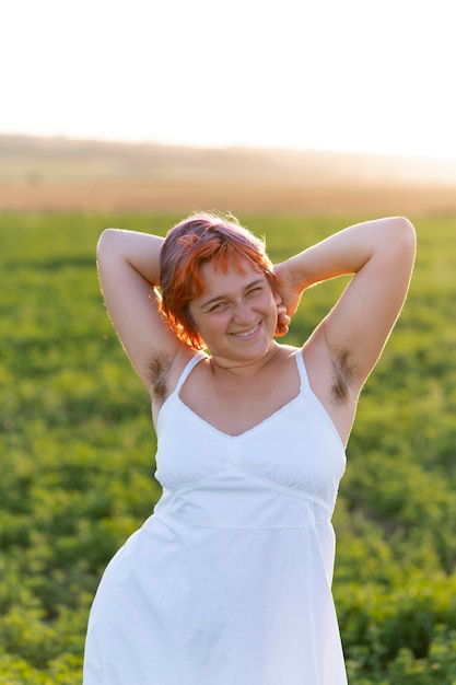 Young woman posing confidently outdoors in a field and showing armpit hair