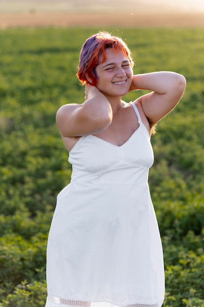 Молодая женщина уверенно позирует на открытом воздухе в поле и показывает волосы подмышками