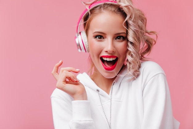 彼女のピンクのヘッドフォンでポーズをとって音楽を聴いている若い女性