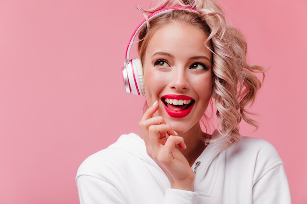 彼女のピンクのヘッドフォンでポーズをとって音楽を聴いている若い女性