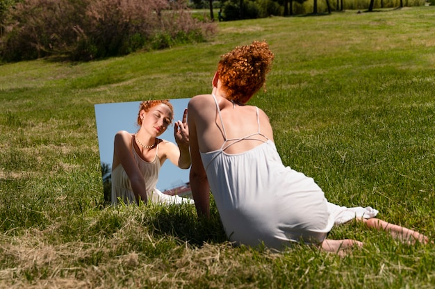 야외 잔디에 거울에 포즈를 취하는 젊은 여자