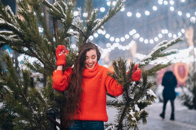 通りのクリスマスツリーの近くでポーズをとって若い女性