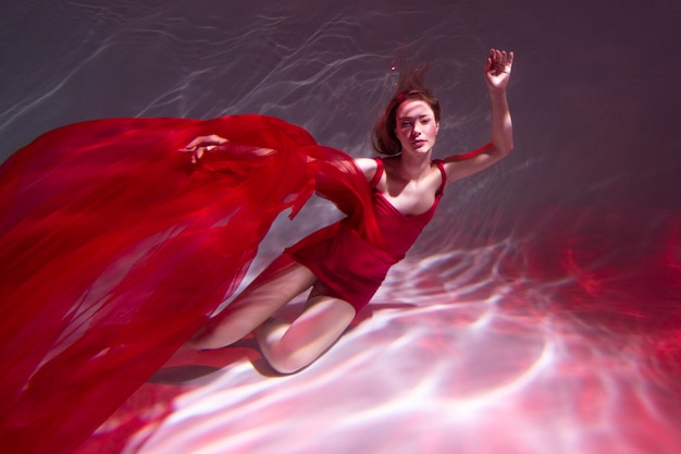 Young woman posing submerged underwater in a flowy dress