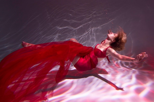 Young woman posing submerged underwater in a flowy dress