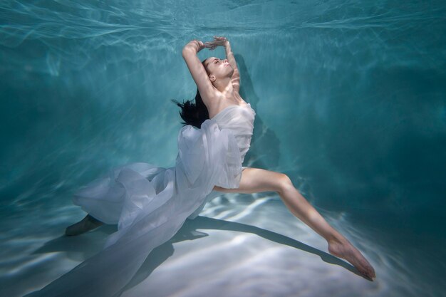 Young woman posing submerged underwater in a flowy dress