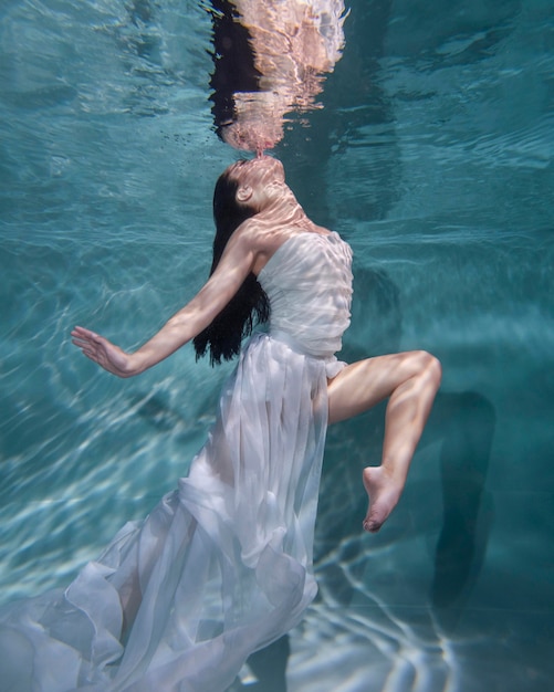 Young woman posing submerged underwater in a flowy dress