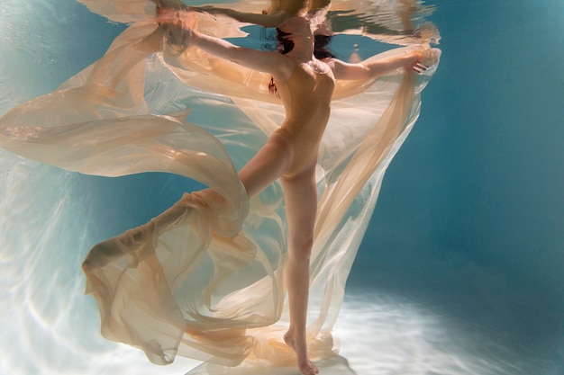 Молодая женщина позирует под водой в струящемся платье