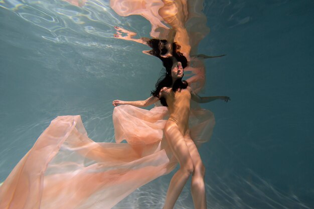 Young woman posing submerged underwater in a flowy dress