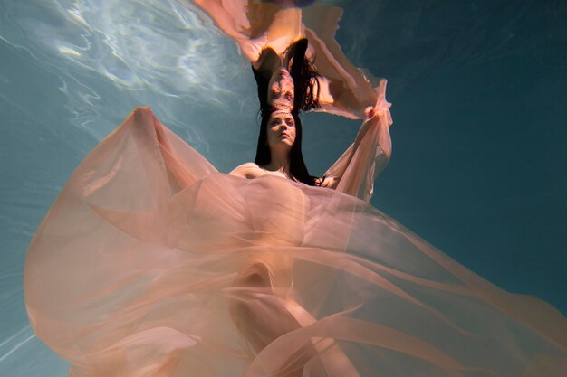 Young woman posing submerged underwater in a flowy dress