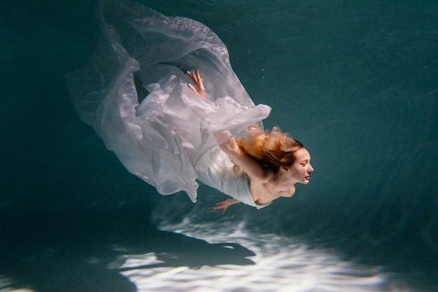 Young woman posing submerged underwater in a flowy dress