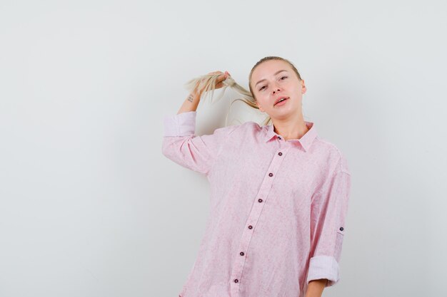 Молодая женщина позирует, держа прядь в розовой рубашке и выглядя красиво