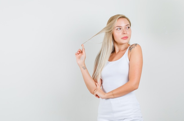 Young woman posing while holding strand with hand in white singlet