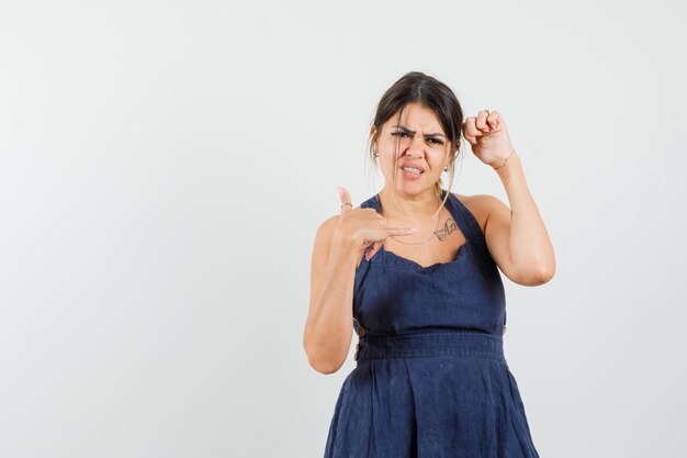 Young woman posing while showing phone gesture in dress and looking gloomy