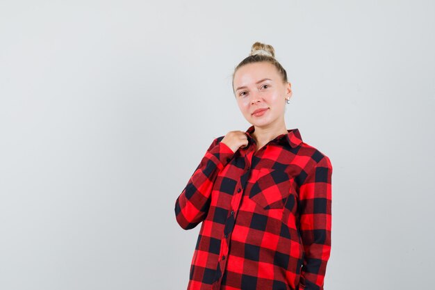 Young woman posing while standing in checked shirt and looking pretty