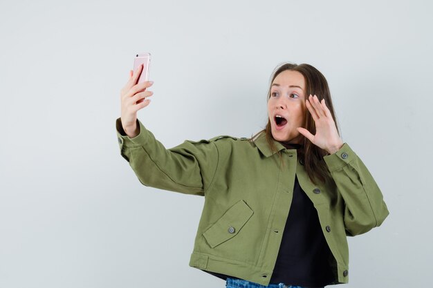 Young woman posing while taking selfie in green jacket front view.