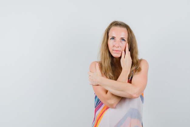 Young woman posing while touching her cheek in summer dress and looking alluring 