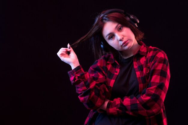 헤드폰을 사용하여 체크 무늬 빨간색과 검은 색 셔츠와 함께 포즈를 취하는 젊은 여자