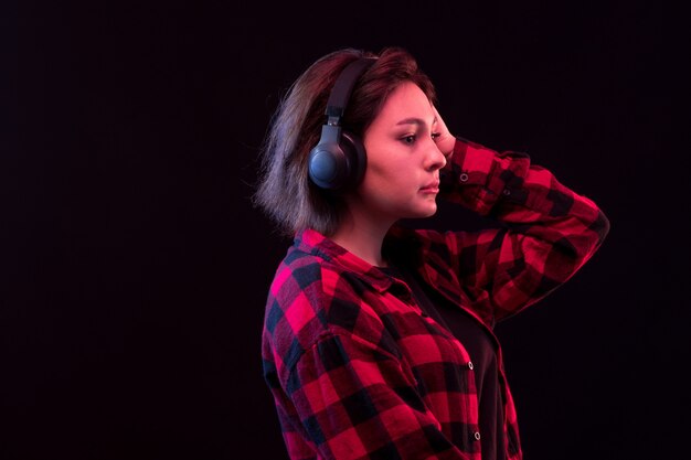 헤드폰을 사용하여 체크 무늬 빨간색과 검은 색 셔츠와 함께 포즈를 취하는 젊은 여자