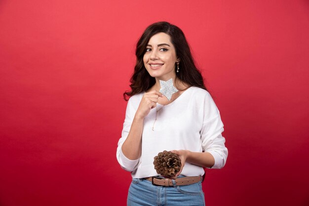 Young woman posing with big Christmas pinecone and star on red background. High quality photo