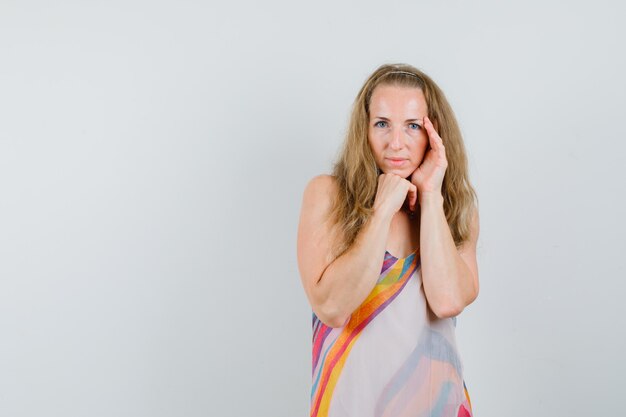 Young woman posing with chin propped on fist in summer dress and looking charming 