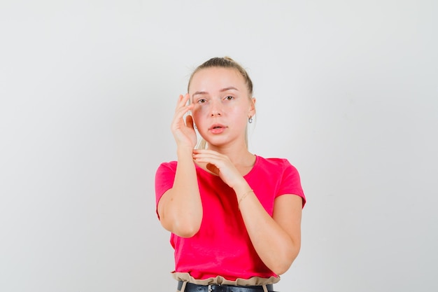 Giovane donna in posa con le mani vicino al viso in t-shirt e sembra carina