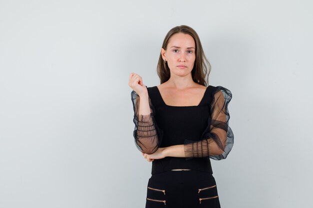 Young woman posing with her elbow on hand in black blouse and looking attractive. front view. space for text