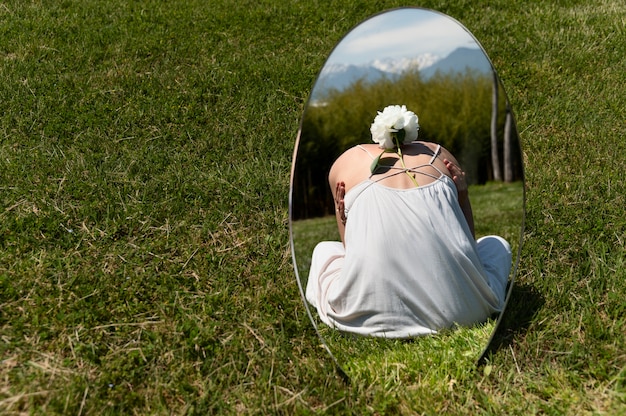 屋外の芝生の上の鏡で牡丹の花でポーズをとる若い女性