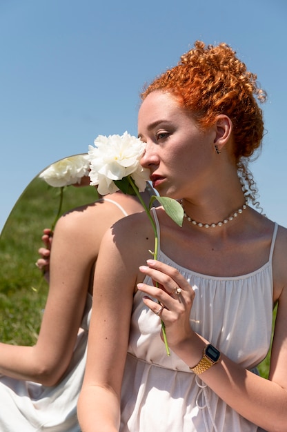 야외 잔디에 거울에 모란 꽃과 함께 포즈를 취하는 젊은 여자