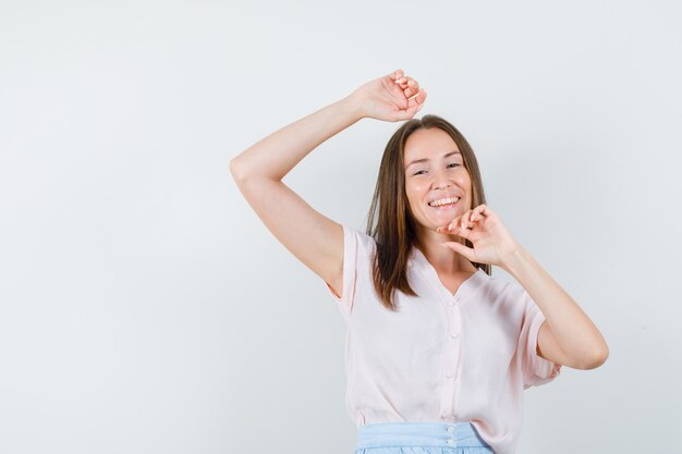 Young woman posing with raised arms in t-shirt, skirt and looking joyful. front view.