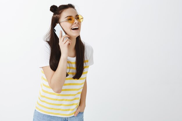 young woman posing with sunglasses and phone against white wall