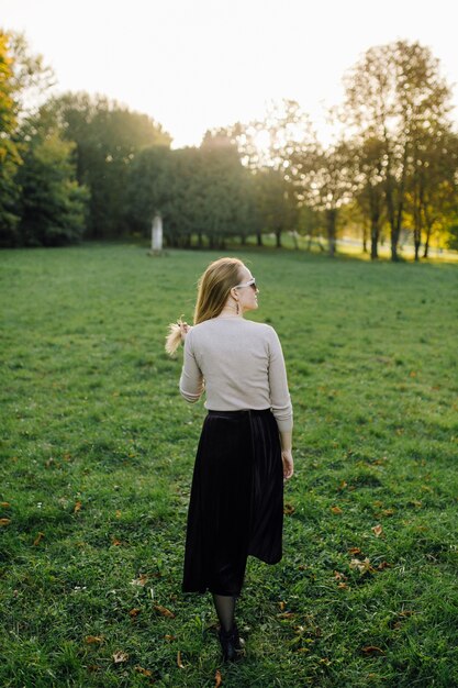 秋の公園で黄色の葉の上にポーズをとる若い女性。アウトドア