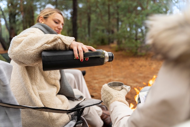 Young woman pouring water in cup for here friend during camp