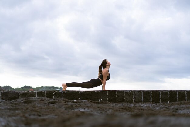 Young woman practice yoga on a beautiful beach at sunrise. Blue sky, ocean, waves, proximity to nature, unity with nature.