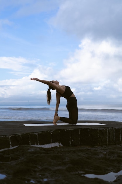 Yoga di pratica della giovane donna su una bella spiaggia all'alba. cielo blu, oceano, onde, vicinanza alla natura, unità con la natura.
