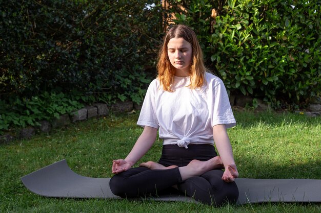 A young woman practices yoga in nature on the grass in the yard