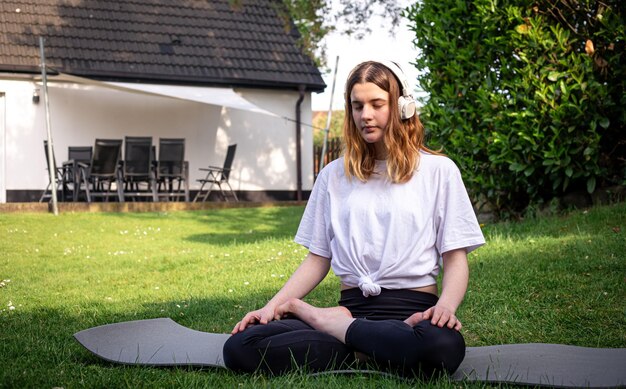 A young woman practices yoga in nature on the grass in the yard